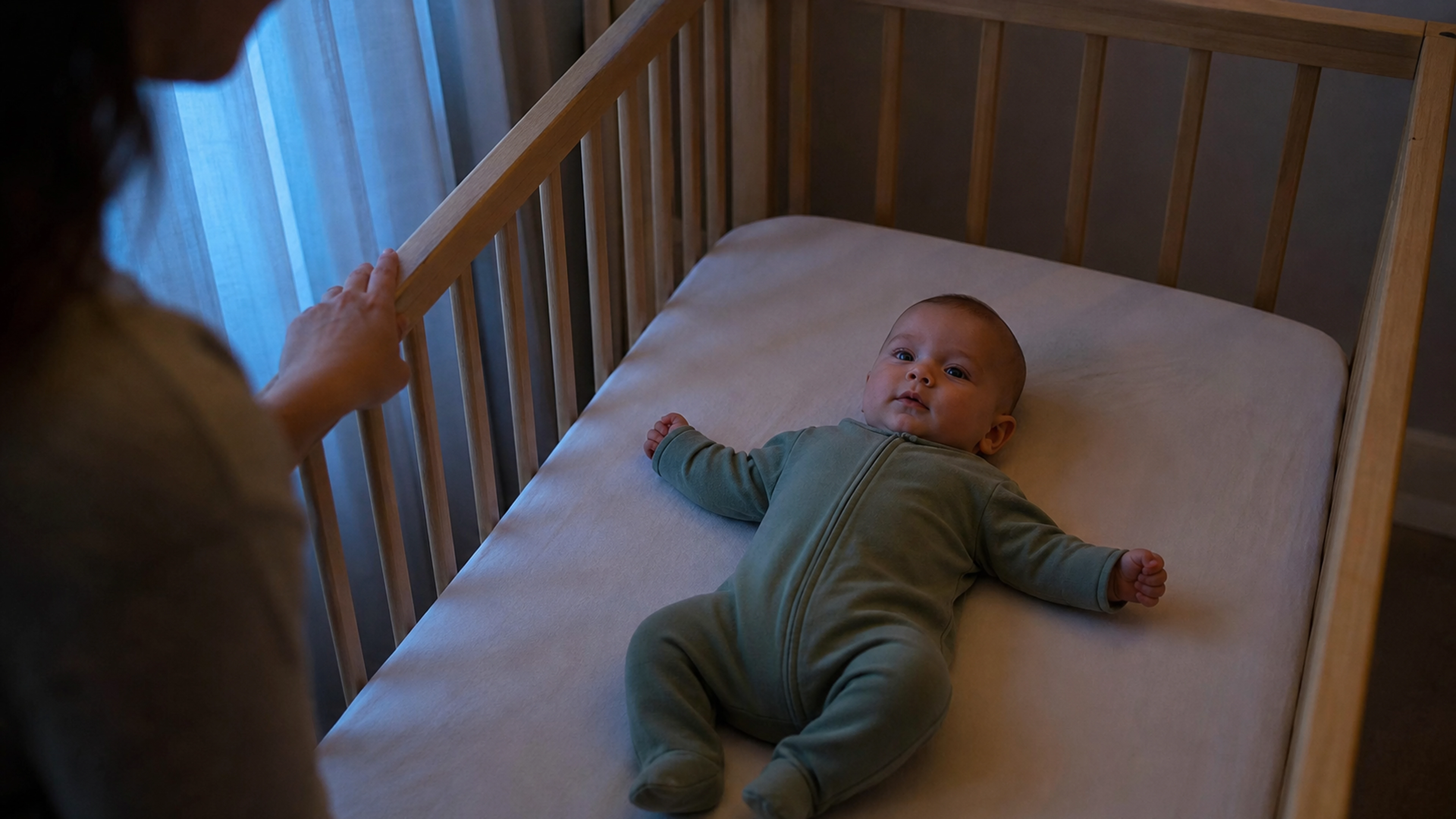 Bébé éveillé allongé sur le dos dans son berceau au coucher, sous le regard d’un parent.