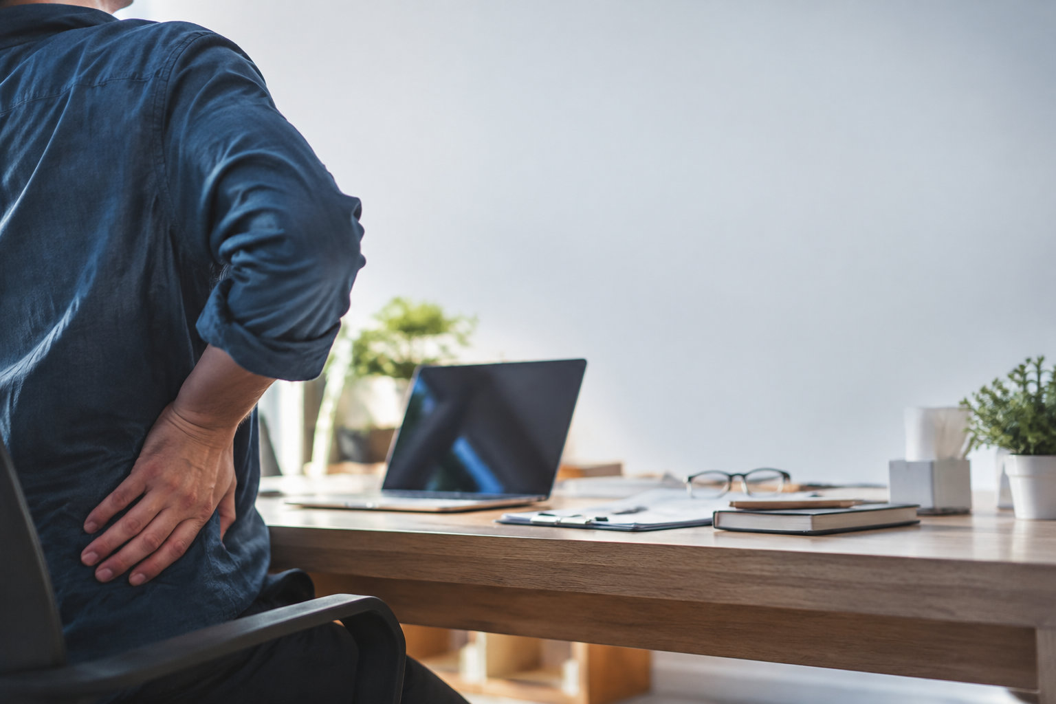 Un employé assis à son bureau tenant son bas du dos avec la main, montrant des signes de douleur physique.
